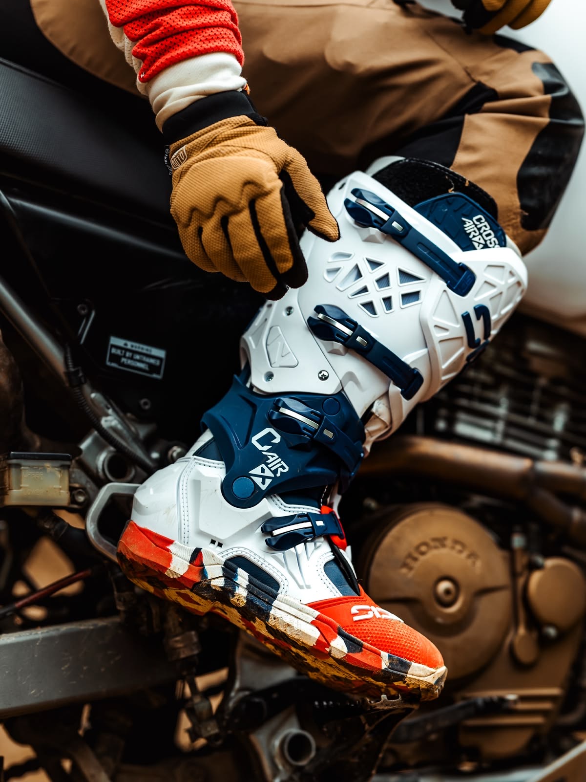 Bota de motocross branca e azul apoiada na pedaleira, com luva de piloto